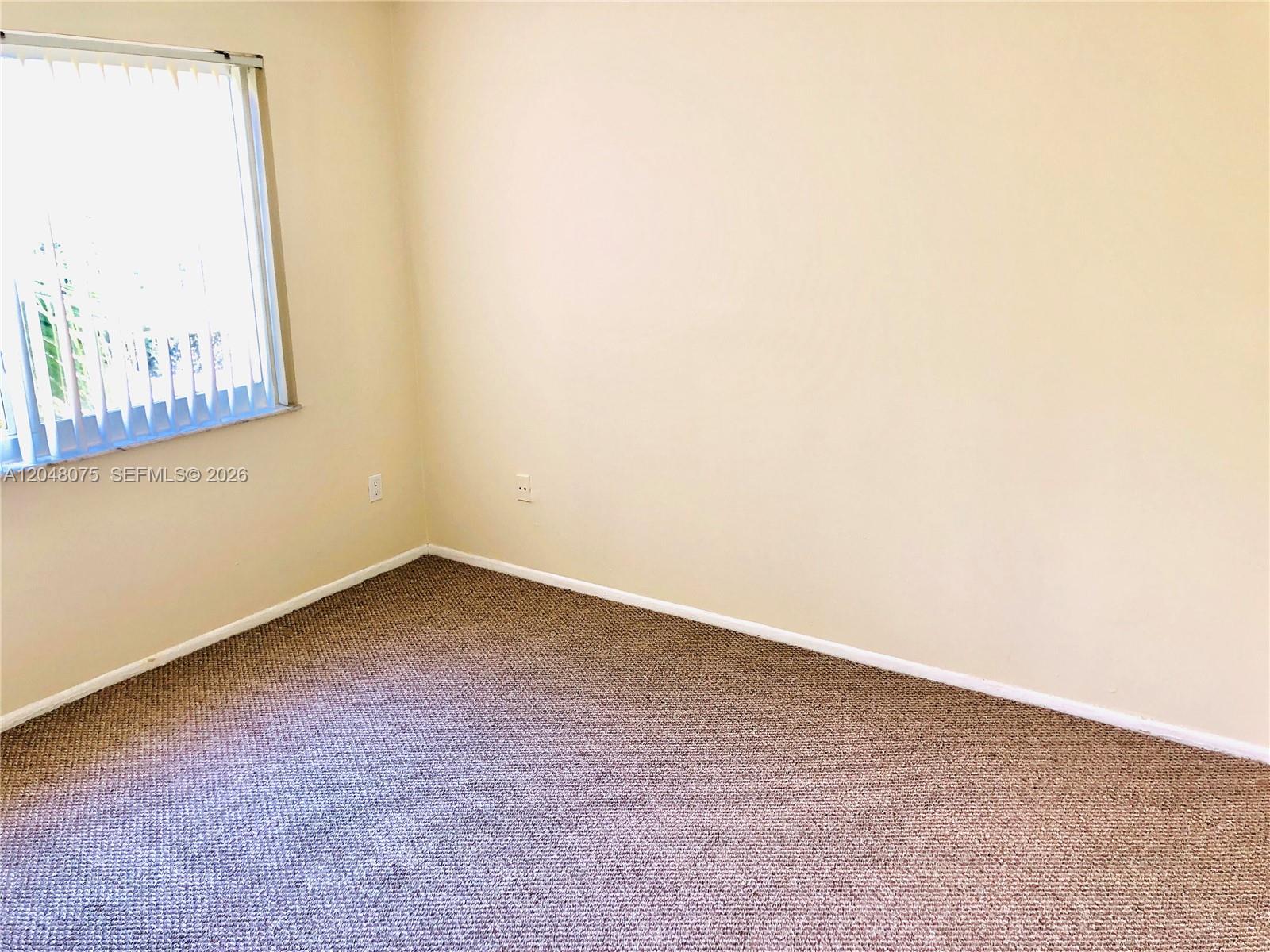 An empty room features beige walls, brown carpeting, and a window with vertical blinds — 7830 Camino Real # K310, Miami FL 33143, MIAMI, FL