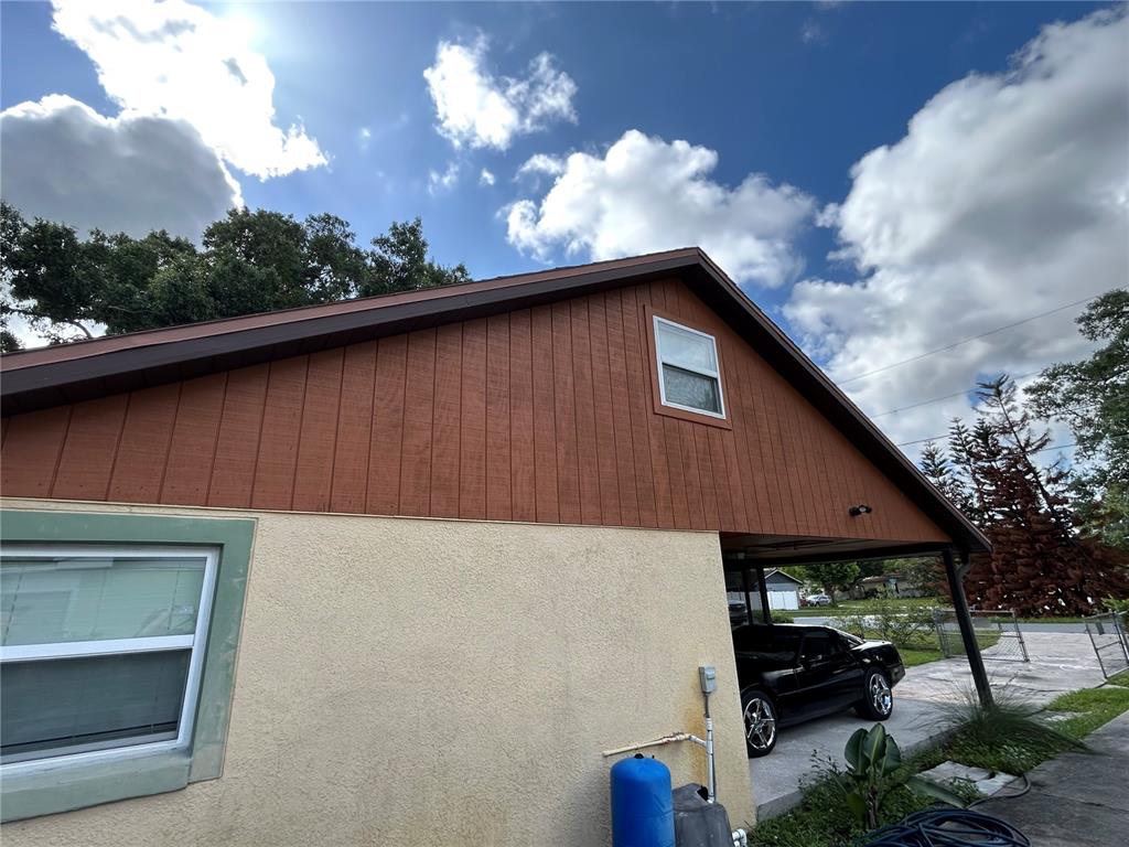 The exterior of a house features a stucco wall, wood-paneled gable, and a covered carport — 1213 CHEROKEE DRIVE, KISSIMMEE, FL