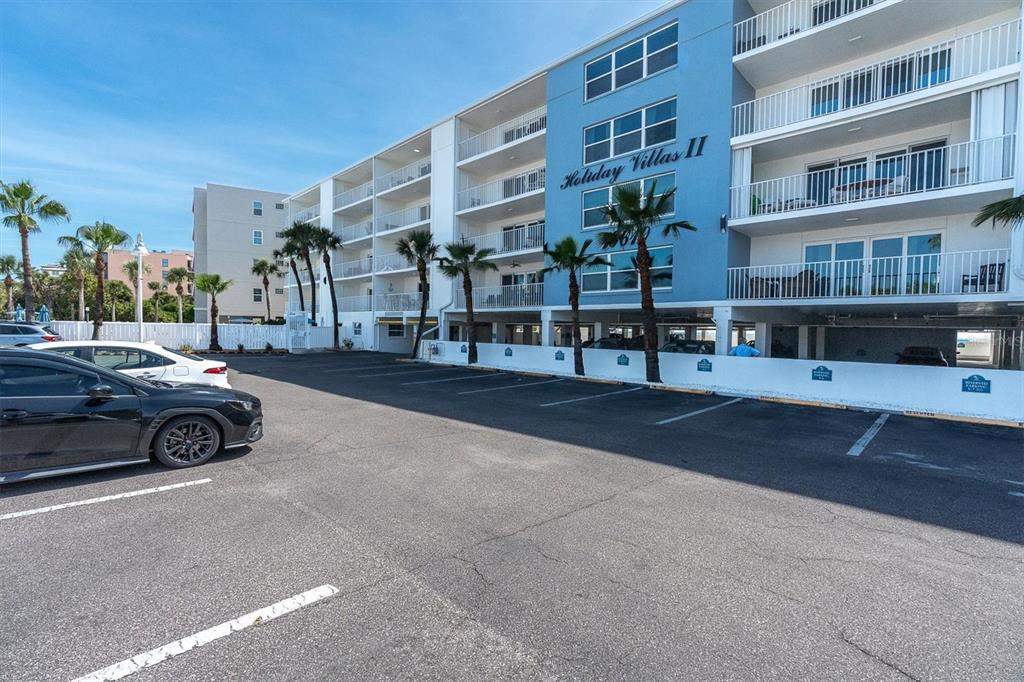 The exterior of a multi-story apartment building features a blue facade and covered parking spaces — 19610 GULF BOULEVARD UNIT 308, INDIAN ROCKS BEACH, FL