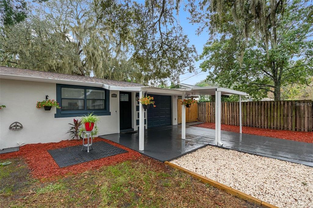 A single-story house exterior features a covered carport, a small patio, and red mulch landscaping — 11115 STAFFORD LANE, RIVERVIEW, FL