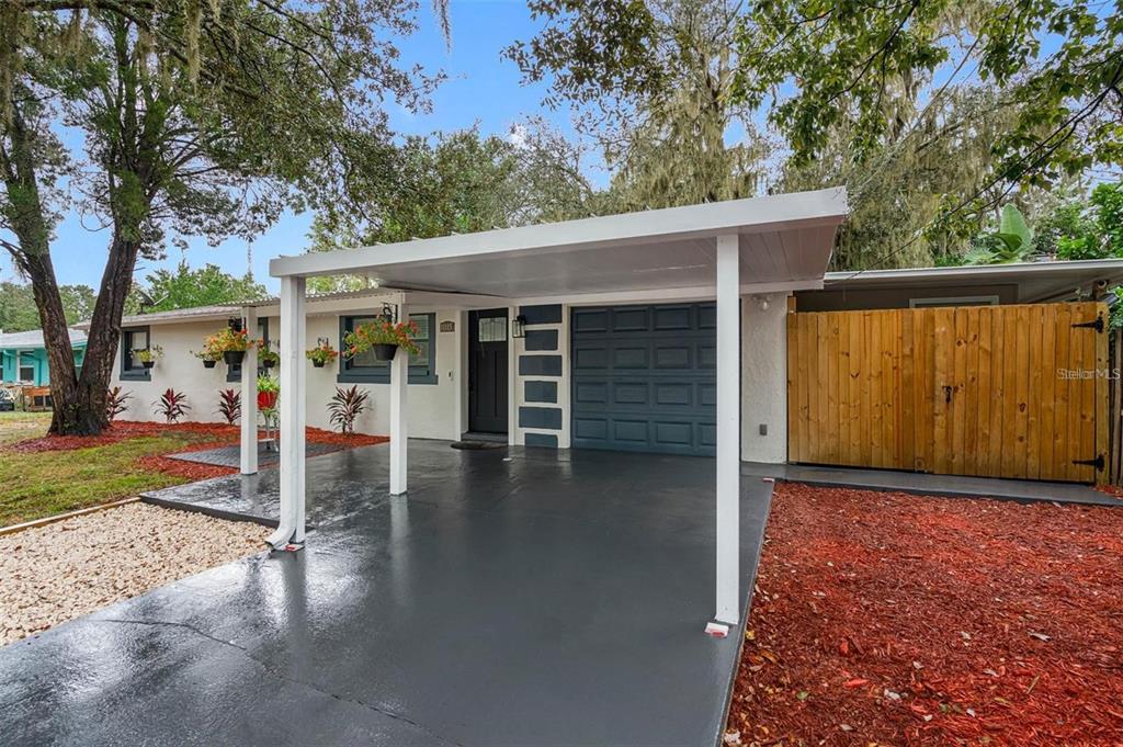 A house exterior features a covered carport, a dark blue garage door, and red mulch landscaping — 11115 STAFFORD LANE, RIVERVIEW, FL