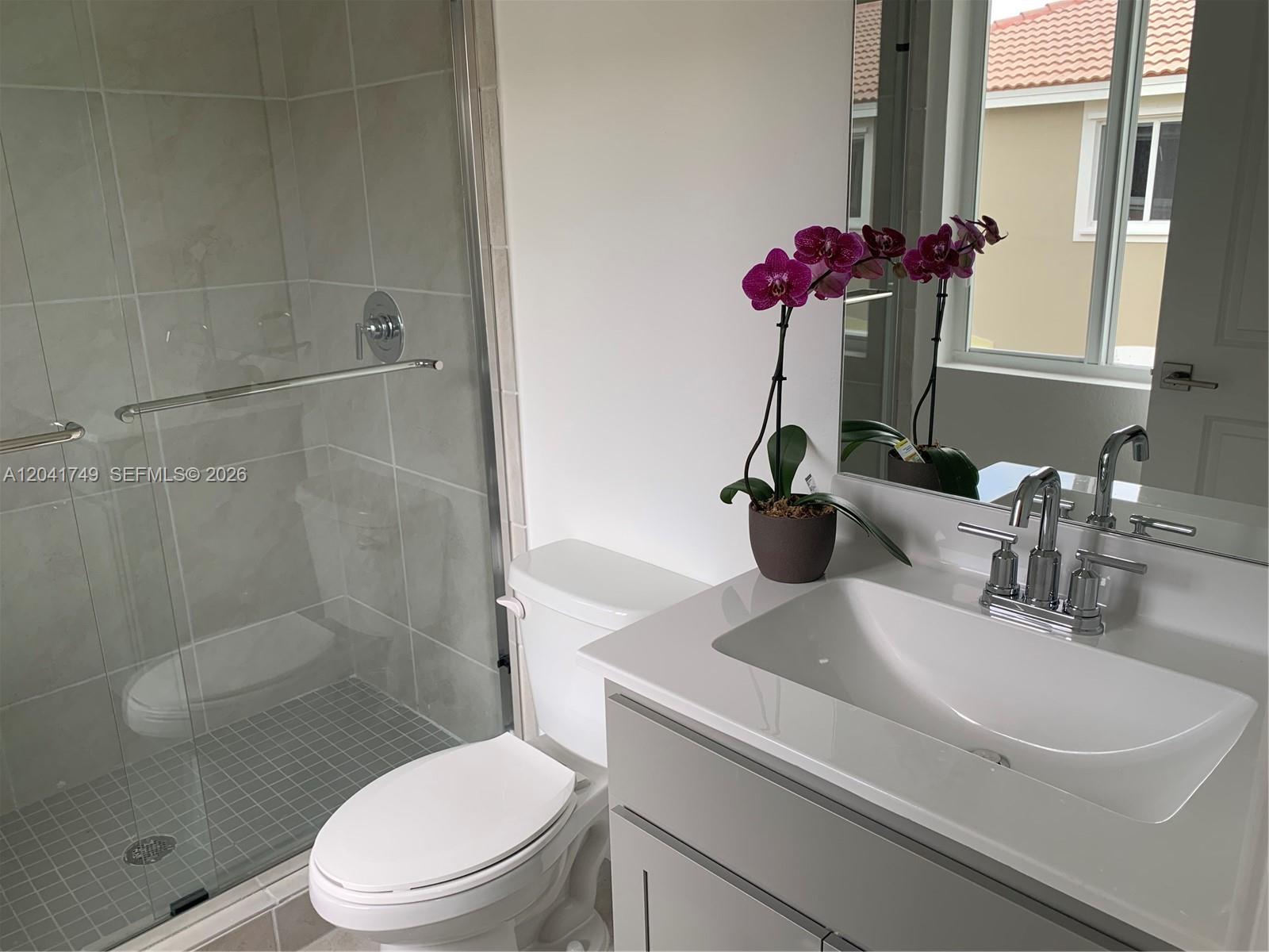 A bathroom features a glass-enclosed shower, a white toilet, and a gray vanity with a sink — 1068 SE 24th Ave # 1068, Homestead FL 33035, HOMESTEAD, FL