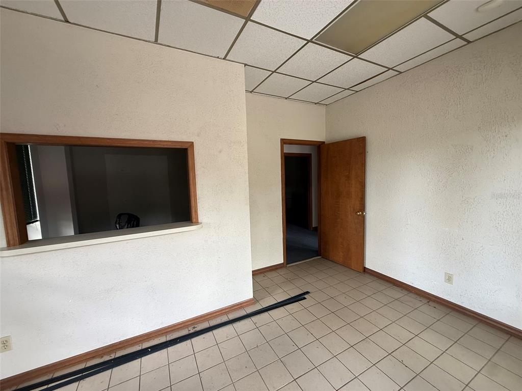 An empty office room features a service window, a wooden door, and tiled flooring — 832 NW 30TH AVENUE UNIT 100 - 300, OCALA, FL