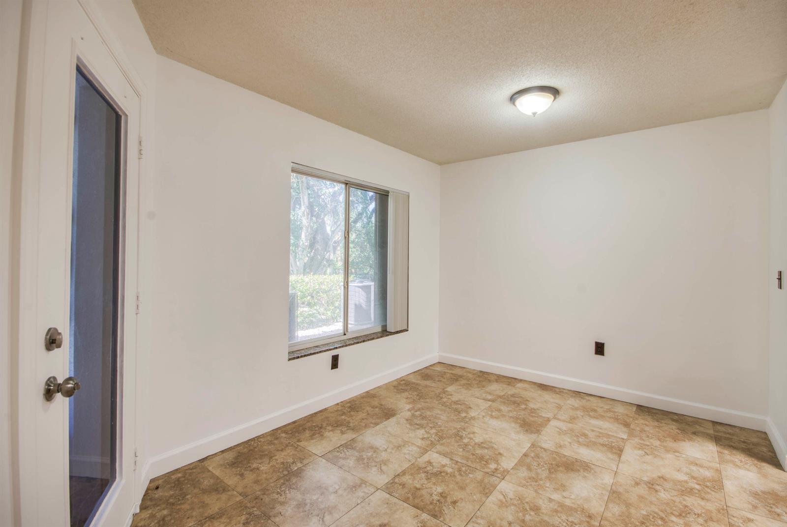 An empty room with white walls, tile flooring, a window, and a glass-paneled door — 815 W Boynton Beach Boulevard # 103, Boynton Beach FL 33426, BOYNTON BEACH, FL