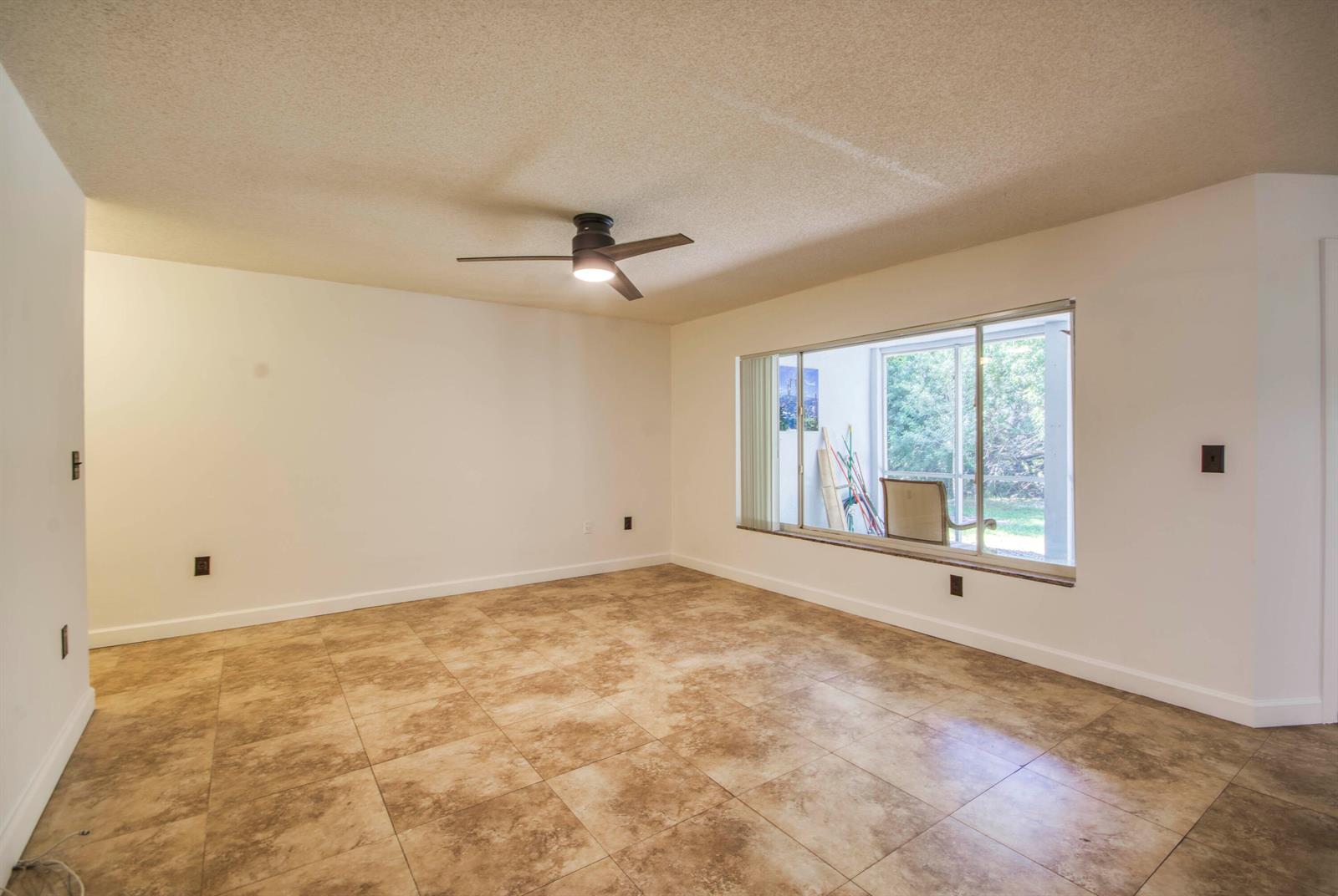 An empty room features beige tile flooring, white walls, a ceiling fan, and a large window — 815 W Boynton Beach Boulevard # 103, Boynton Beach FL 33426, BOYNTON BEACH, FL