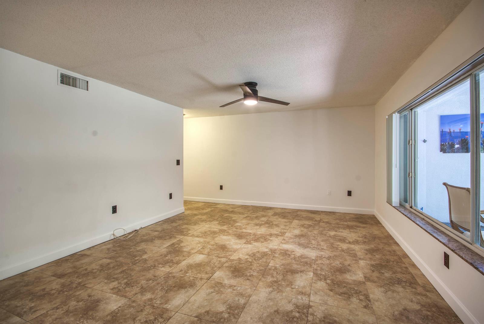 An empty room with beige tile flooring, white walls, a ceiling fan, and a large window — 815 W Boynton Beach Boulevard # 103, Boynton Beach FL 33426, BOYNTON BEACH, FL