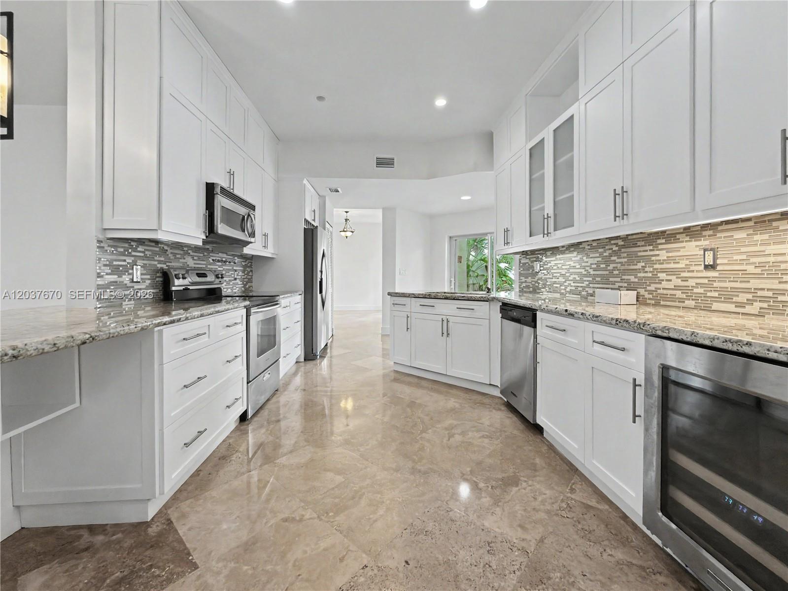 A modern kitchen features white cabinetry, granite countertops, stainless steel appliances, and polished stone flooring — 4725 NW 104th Ave, Doral FL 33178, DORAL, FL
