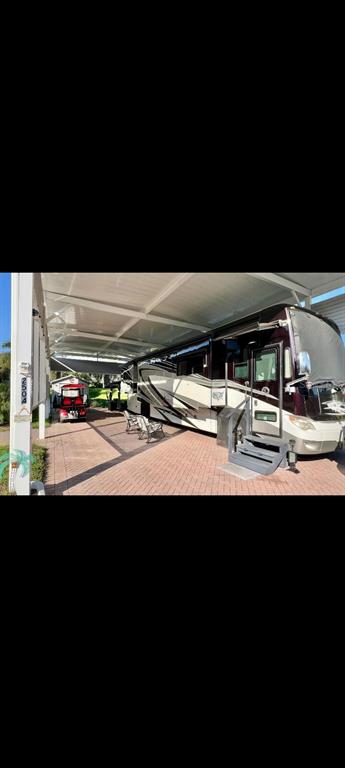 A large recreational vehicle is parked under a metal carport on a paved driveway — 2504 ST GEORGE DRIVE, DAVENPORT, FL