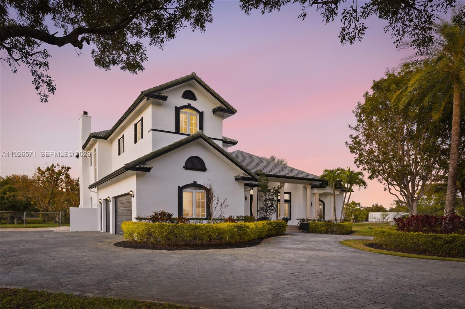 A two-story white house with dark trim and a paved driveway at sunset — 20401 SW 48th Pl, Southwest Ranches FL 33332, SOUTHWEST RANCHES, FL