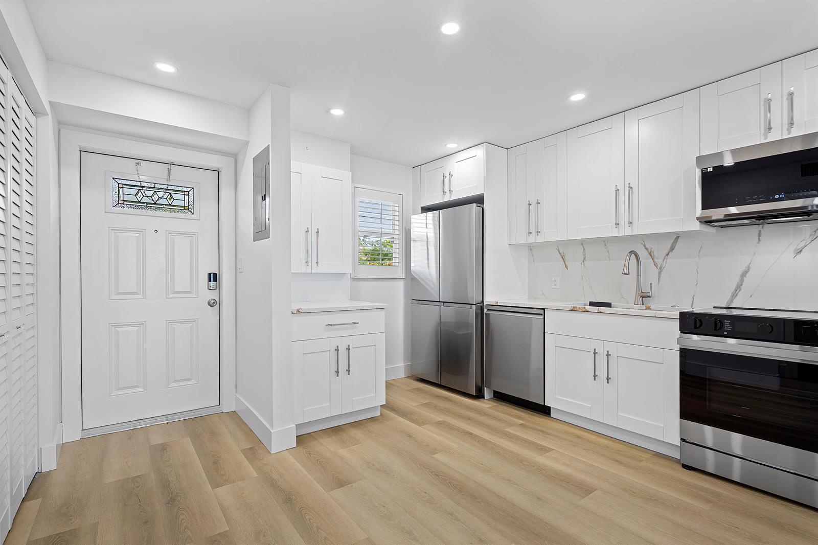 A modern kitchen features white cabinets, stainless steel appliances, and light wood-look flooring — 750 NE Spanish River Boulevard # 1090, Boca Raton FL 33431, BOCA RATON, FL