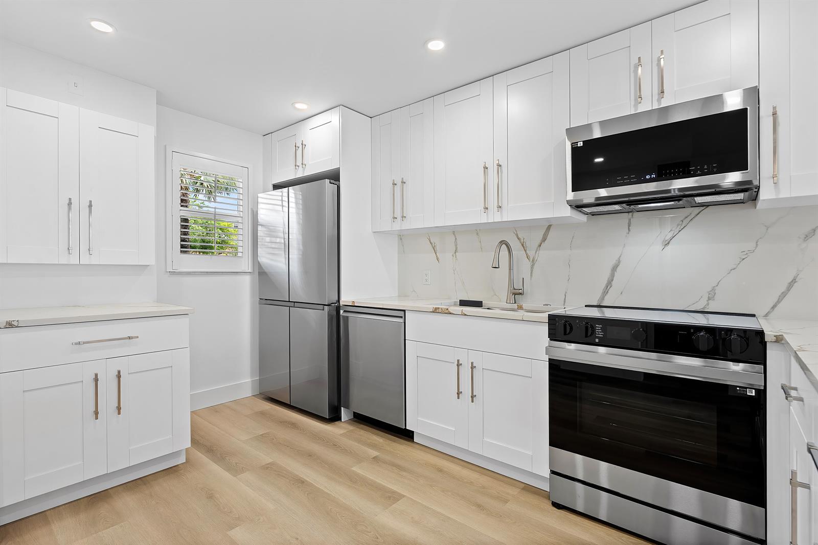A modern kitchen features white cabinetry, stainless steel appliances, and a marble-patterned backsplash — 750 NE Spanish River Boulevard # 1090, Boca Raton FL 33431, BOCA RATON, FL