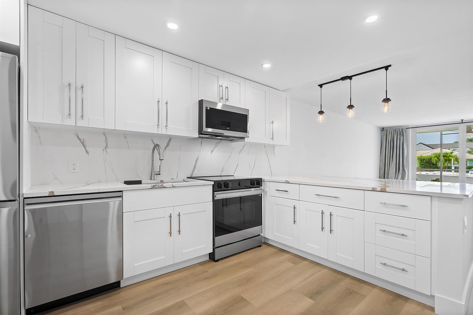 A modern kitchen features white shaker cabinets, stainless steel appliances, and marble-look countertops — 750 NE Spanish River Boulevard # 1090, Boca Raton FL 33431, BOCA RATON, FL