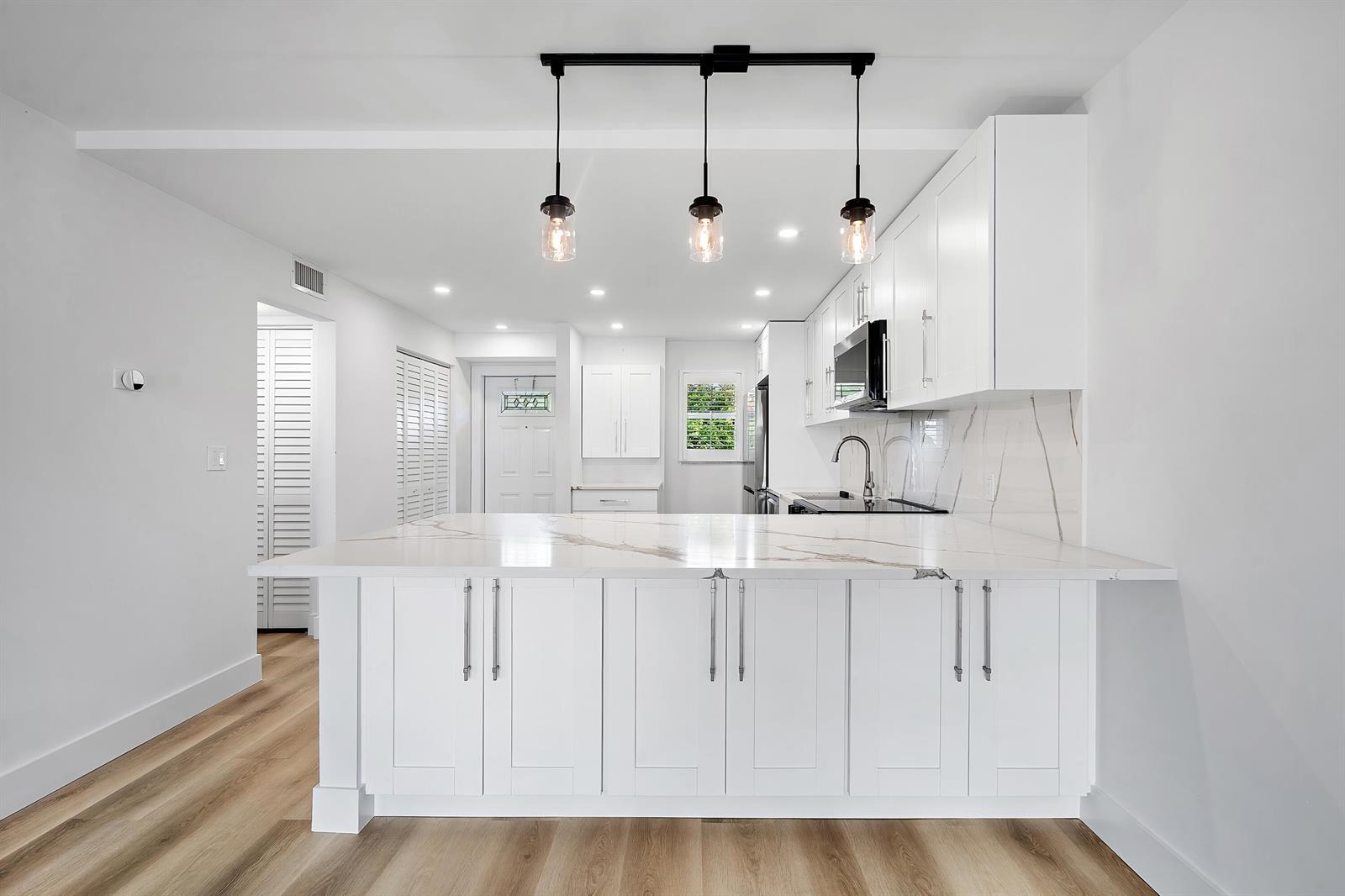 A modern white kitchen features a marble-topped island, pendant lighting, and light wood flooring — 750 NE Spanish River Boulevard # 1090, Boca Raton FL 33431, BOCA RATON, FL