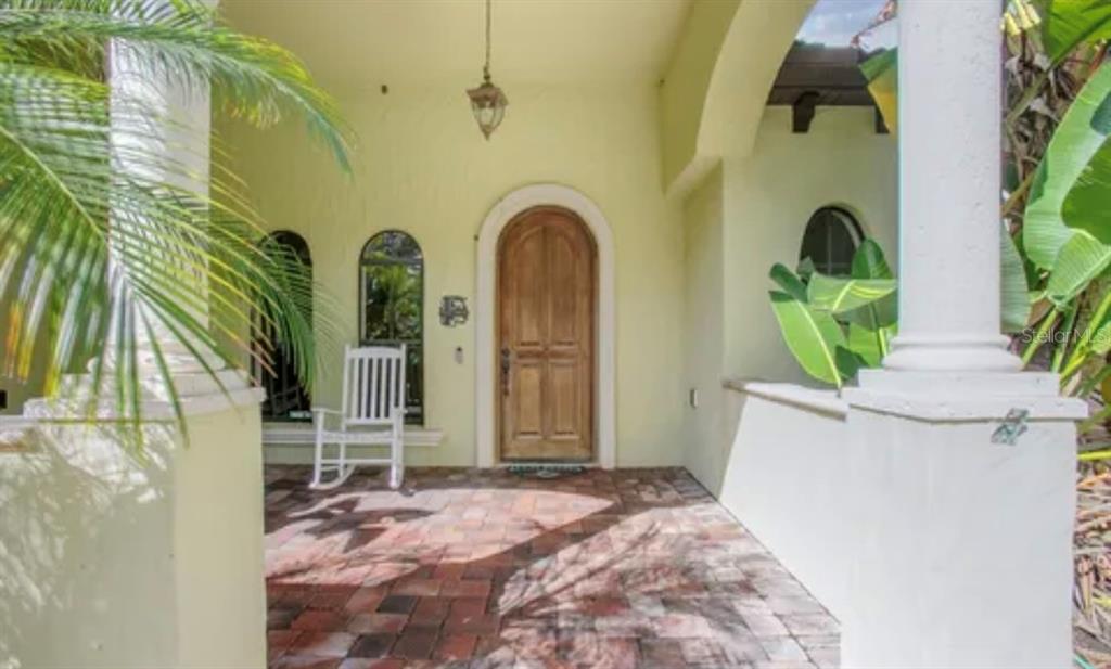 A covered porch features a brick floor, a wooden arched door, and a white rocking chair — 100 VIA ROSA COURT, DEBARY, FL