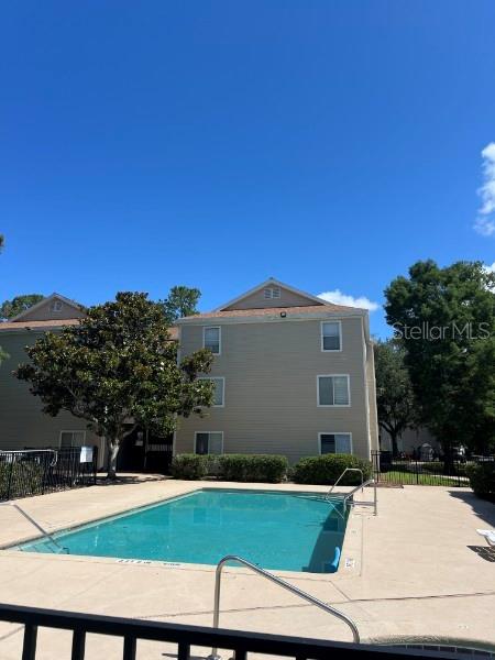 A swimming pool sits in front of a three-story apartment building under a blue sky — 3800 SW 20TH AVENUE UNIT 204-Rm 4, GAINESVILLE, FL