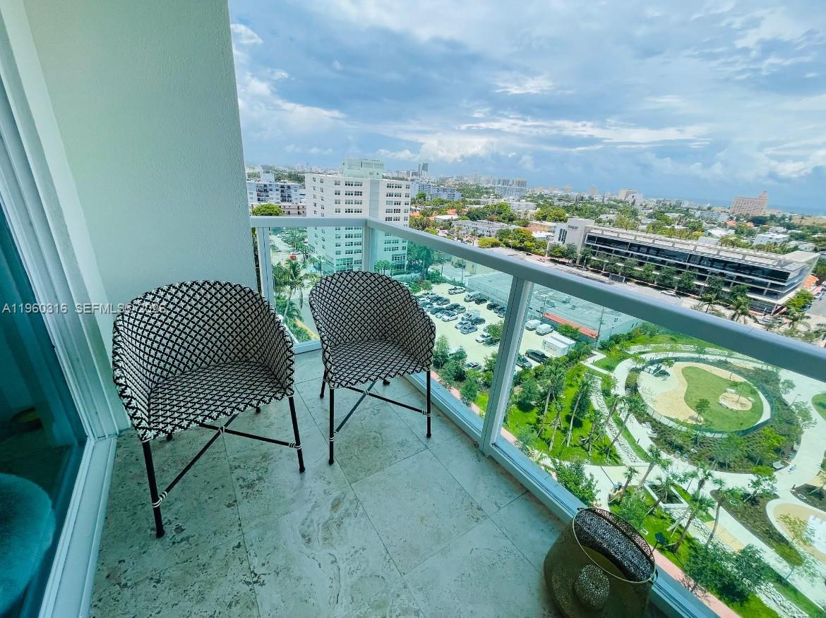 A balcony with two patterned chairs overlooks a park, parking lot, and city skyline — 650 West Ave # 1704, Miami Beach FL 33139, MIAMI BEACH, FL