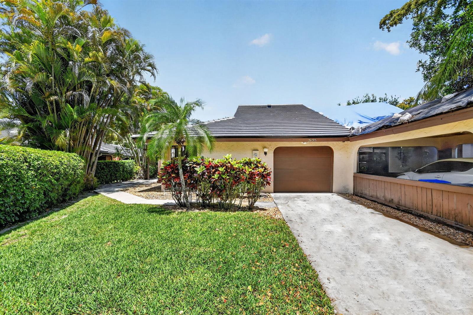A single-story house with a brown garage door, a concrete driveway, and lush tropical landscaping — 5155 Pine Drive, Boynton Beach FL 33437, BOYNTON BEACH, FL