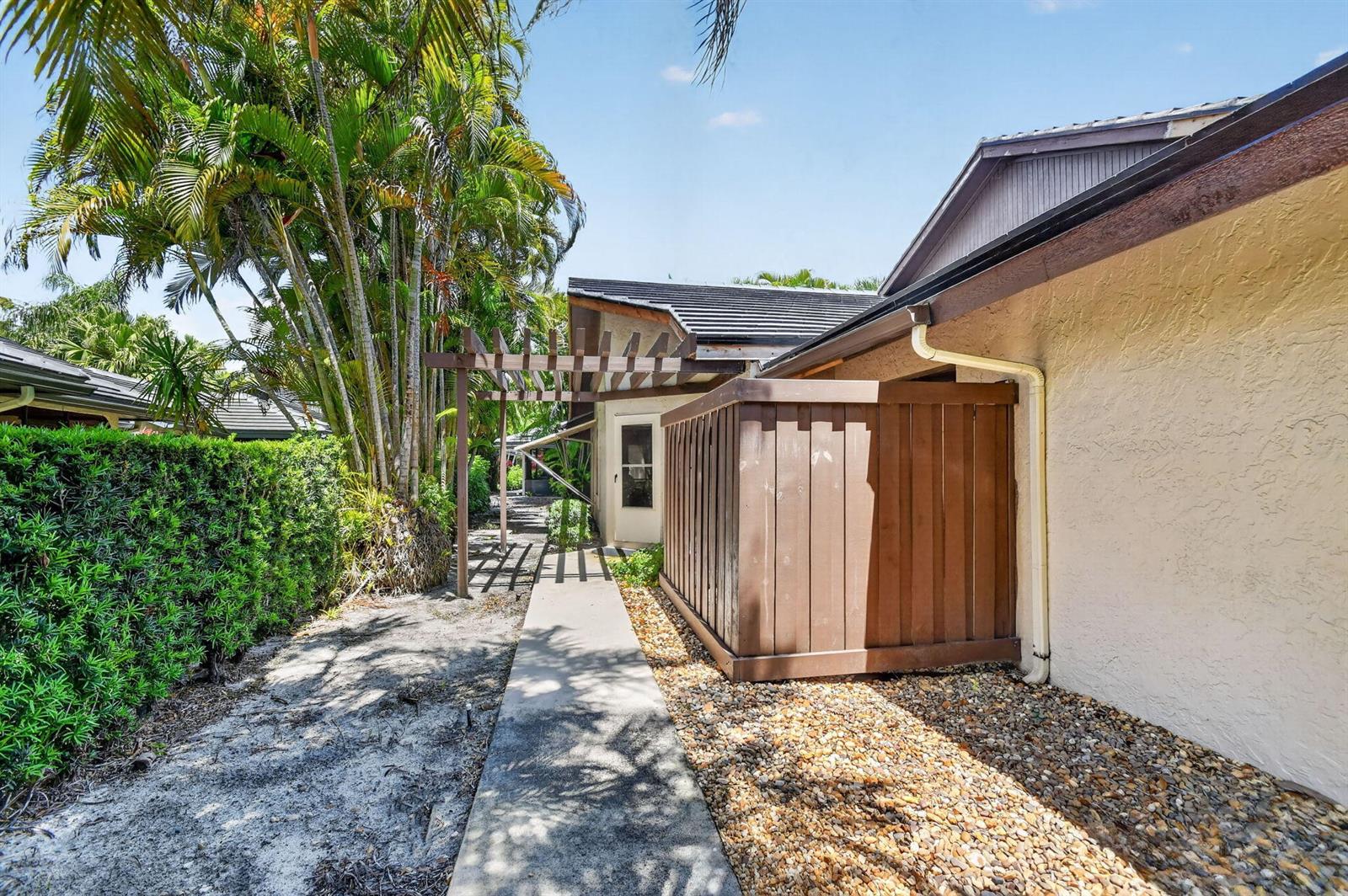 A concrete walkway leads past a wooden privacy screen toward a house exterior with landscaping — 5155 Pine Drive, Boynton Beach FL 33437, BOYNTON BEACH, FL