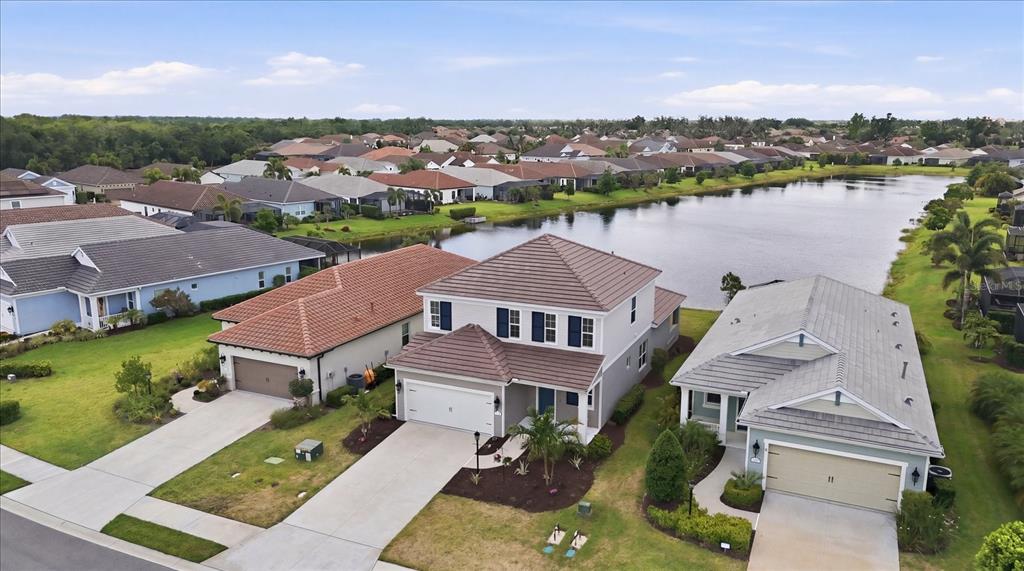 An aerial view shows three suburban houses with tiled roofs situated along a small lake — 12708 AQUAMARINE AVENUE, BRADENTON, FL
