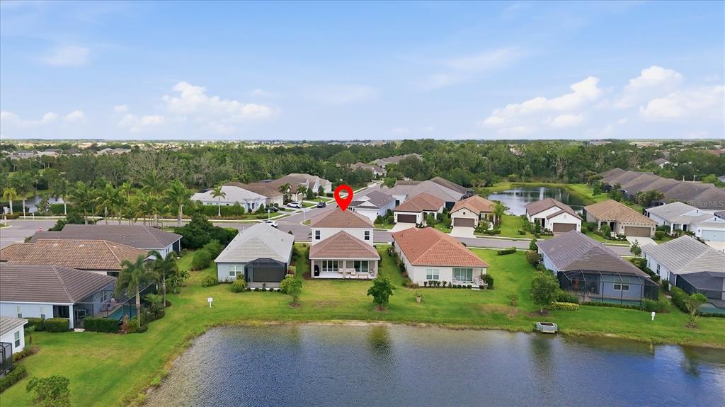 An aerial view shows a two-story house with a red-tiled roof beside a lake — 12708 AQUAMARINE AVENUE, BRADENTON, FL