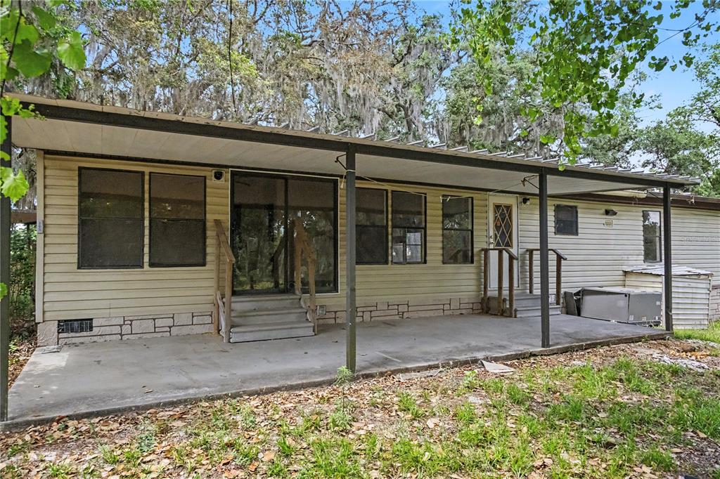 A single-story house with light-colored siding, a concrete patio, and a covered porch — 18007 SE 90TH STREET, OCKLAWAHA, FL