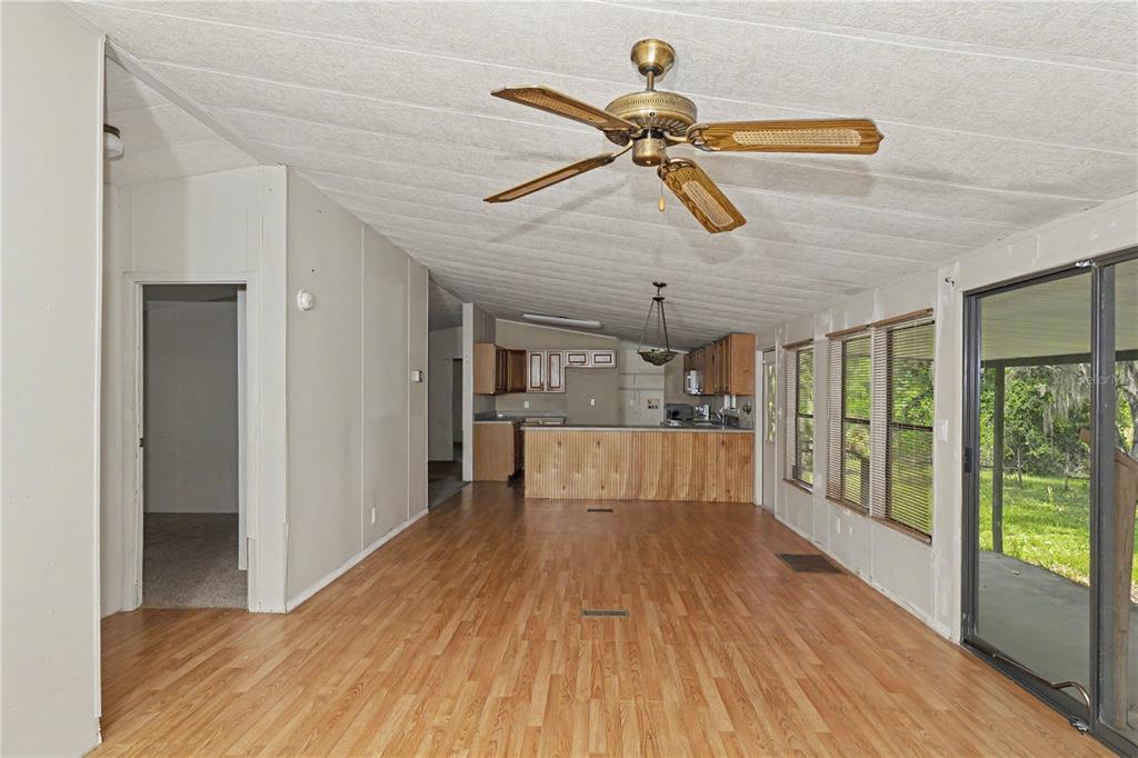 A living room with wood-look flooring, a ceiling fan, and an open kitchen beyond — 18007 SE 90TH STREET, OCKLAWAHA, FL