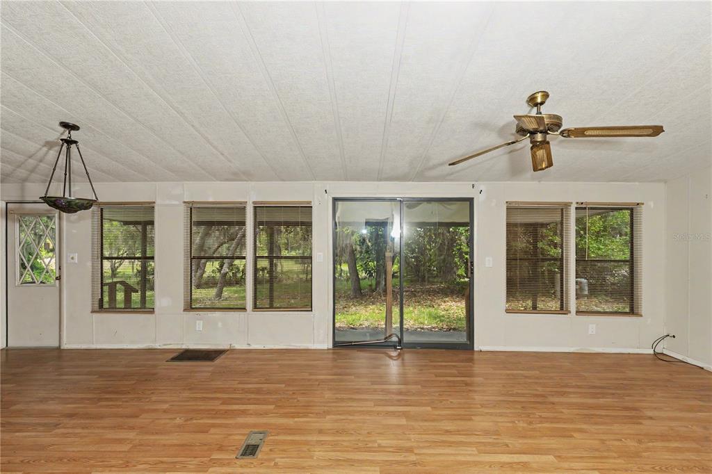 A room with wood-look flooring, a ceiling fan, sliding glass doors, and multiple windows — 18007 SE 90TH STREET, OCKLAWAHA, FL