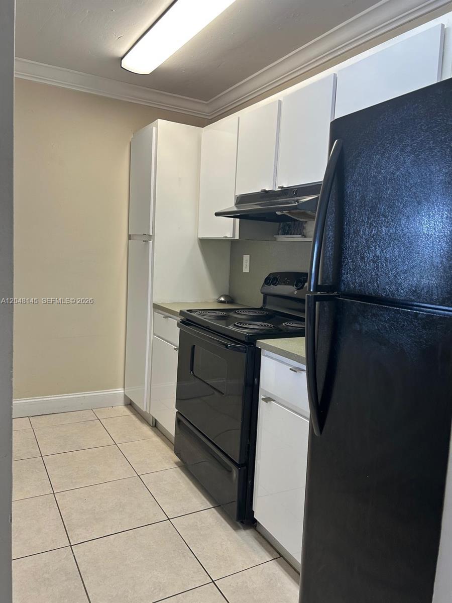 A galley-style kitchen features white cabinets, black appliances, and light-colored floor tiles — 6955 NW 186th St # F505, Hialeah FL 33015, HIALEAH, FL