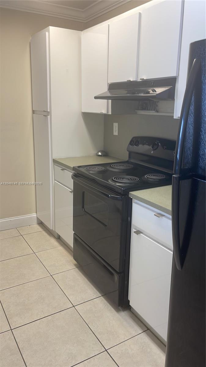 A kitchen features white cabinets, a black stove, a black refrigerator, and light-colored tile flooring — 6955 NW 186th St # F505, Hialeah FL 33015, HIALEAH, FL