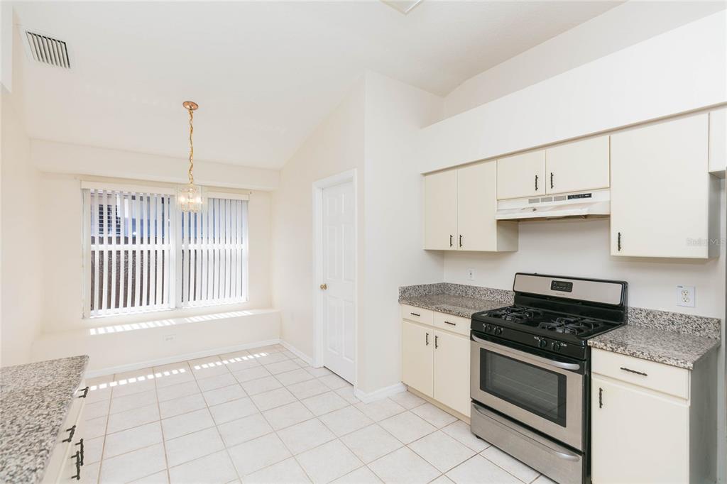 A kitchen with light cabinets, granite countertops, stainless steel appliances, and a dining area — 22704 RODERICK DRIVE, LAND O LAKES, FL