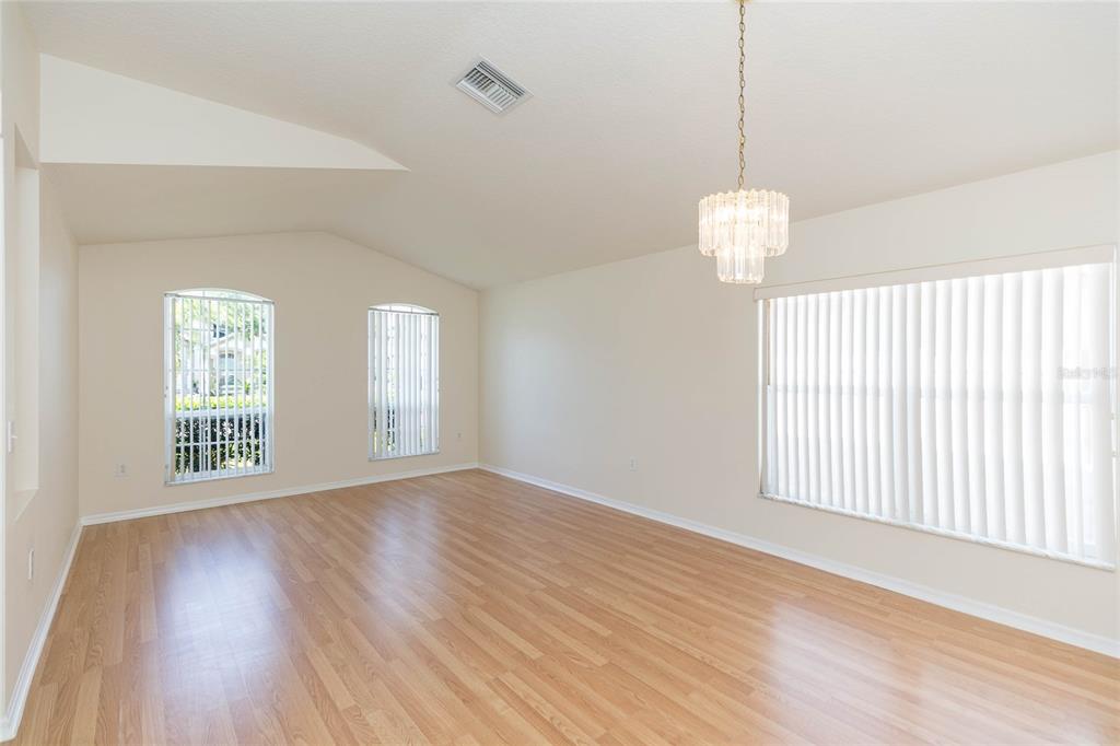 An empty room with light wood flooring, a crystal chandelier, and vertical window blinds — 22704 RODERICK DRIVE, LAND O LAKES, FL