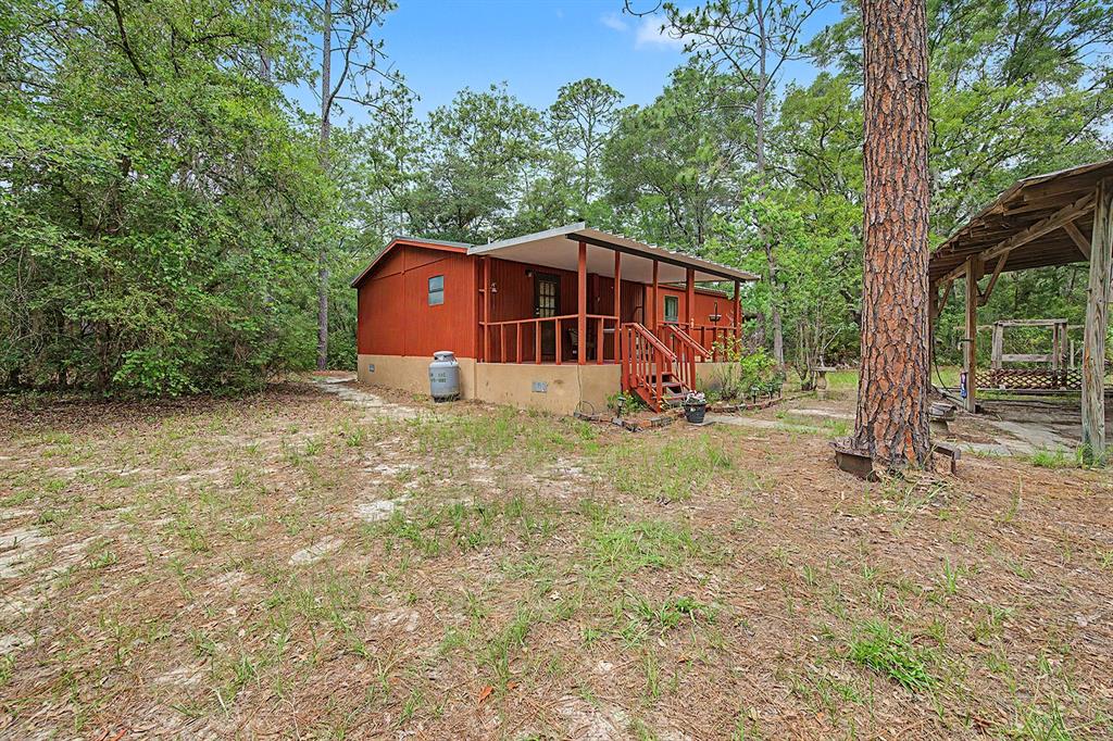 A small, red-sided cabin with a covered front porch sits in a wooded yard — 550 NW 73RD WAY, BELL, FL