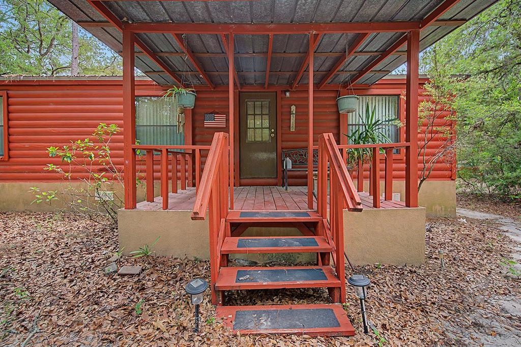 A red log-style cabin features a covered front porch with wooden stairs and railings — 550 NW 73RD WAY, BELL, FL