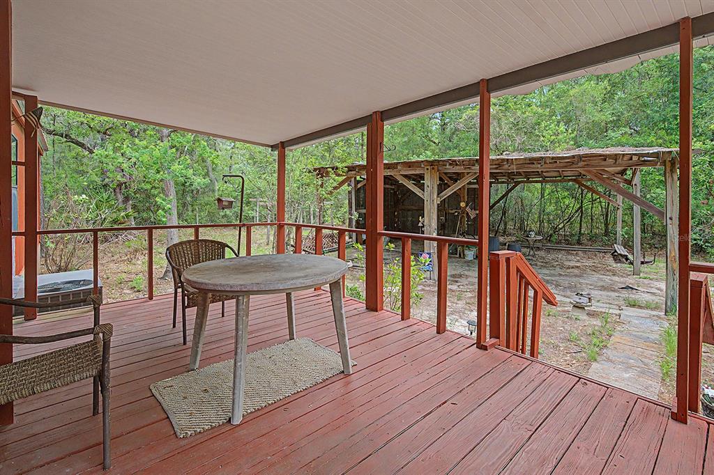 A covered wooden deck features a round table and chairs overlooking a wooded backyard area — 550 NW 73RD WAY, BELL, FL