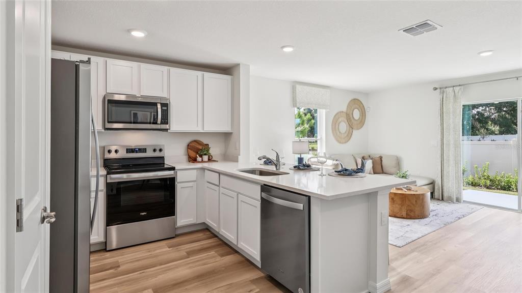 A modern kitchen with white cabinets and stainless steel appliances opens into a living area — 8304 GOWER TRAIL, WILDWOOD, FL