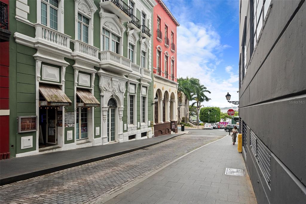 A cobblestone street lined with historic green and red buildings leads toward a waterfront view — 301 SAN JUSTO, SAN JUAN, PR