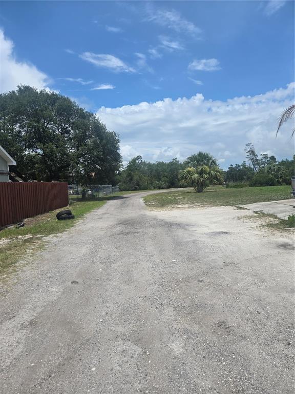 A gravel driveway leads toward a wooded area under a blue sky with clouds — 3120 LORI COURT, DELTONA, FL