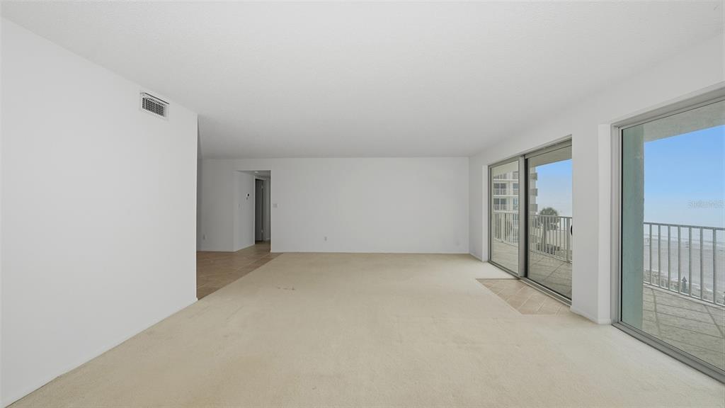 An empty living room with beige carpet, white walls, and sliding glass doors to a balcony — 2301 GULF OF MEXICO DRIVE UNIT 43N, LONGBOAT KEY, FL