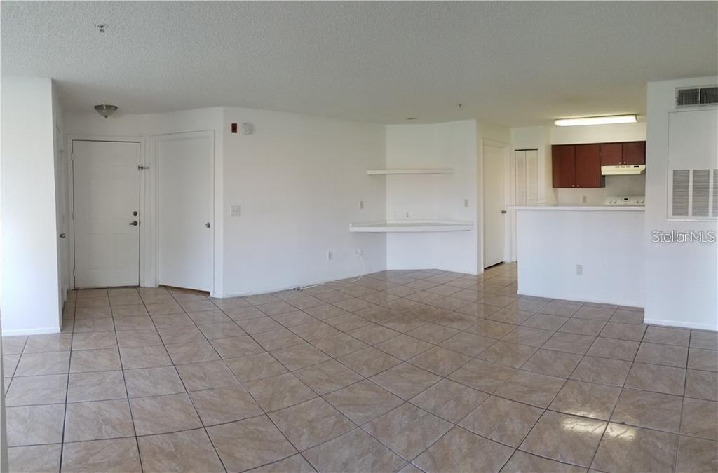 An open-concept living area features light-colored tile flooring, white walls, and a small kitchen — 2213 GRAND CAYMAN COURT UNIT 1128, KISSIMMEE, FL