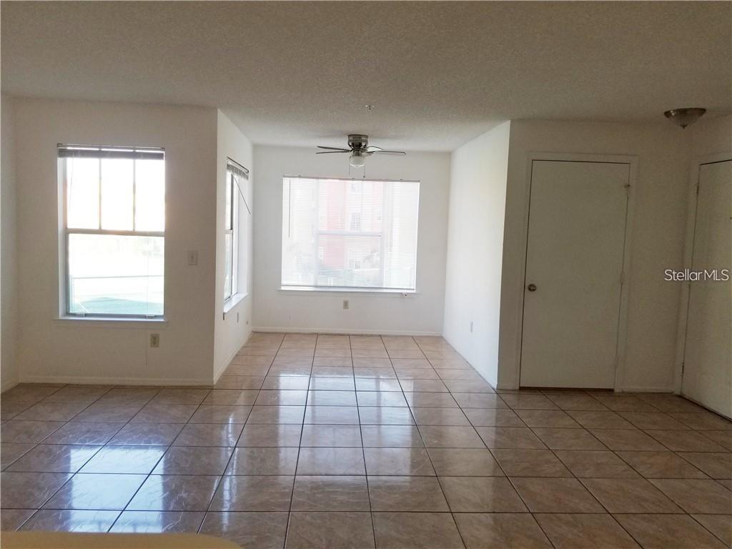 An empty room with beige tile flooring, white walls, a ceiling fan, and multiple windows — 2213 GRAND CAYMAN COURT UNIT 1128, KISSIMMEE, FL