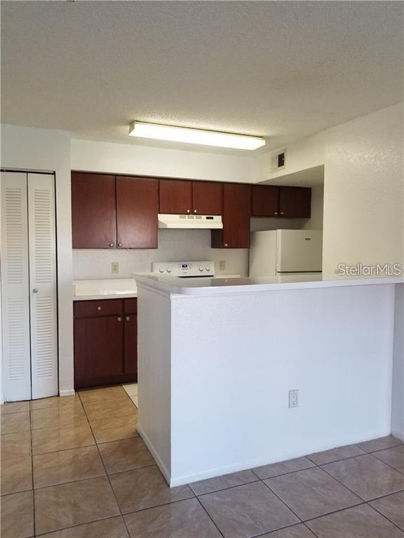 A kitchen features dark wood cabinets, white countertops, a white refrigerator, and tiled flooring — 2213 GRAND CAYMAN COURT UNIT 1128, KISSIMMEE, FL