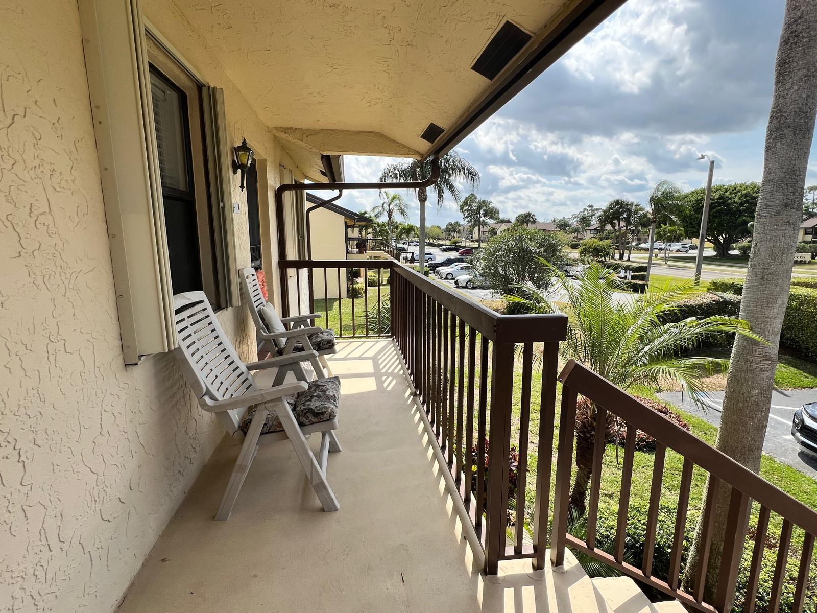 A covered balcony features two white chairs, brown railings, and a view of a parking lot — 4682 Lucerne Lakes Boulevard # 206, Lake Worth FL 33467, LAKE WORTH, FL