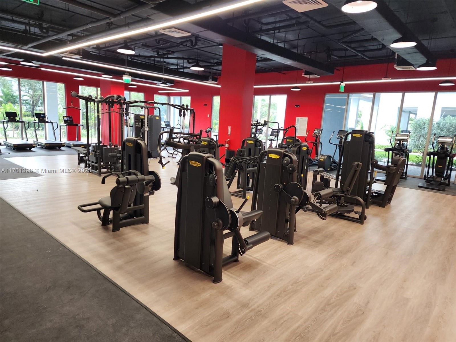 A gym features black exercise machines, light wood flooring, and red accent walls — 7825 NW 107th Ave # 718, Doral FL 33178, DORAL, FL