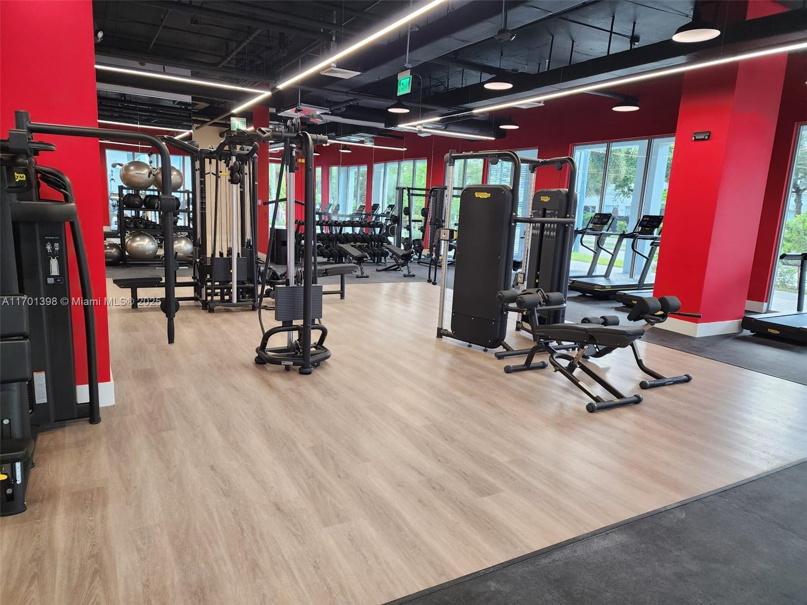 This gym features wood-look flooring, red accent walls, and various strength training and cardio equipment — 7825 NW 107th Ave # 718, Doral FL 33178, DORAL, FL