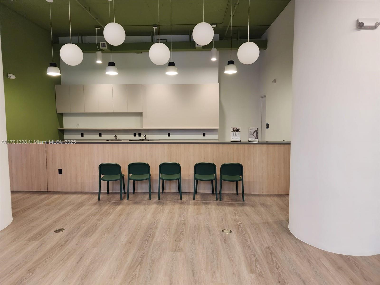 A modern kitchen area features light wood cabinetry, five green chairs, and globe pendant lighting — 7825 NW 107th Ave # 718, Doral FL 33178, DORAL, FL
