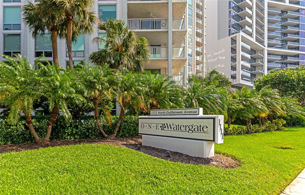 A sign for One Watergate stands in front of a multi-story residential building with palm trees — 1111 N GULFSTREAM AVE #1A AVENUE UNIT 1A, SARASOTA, FL