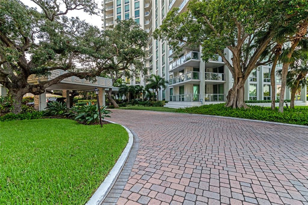 A paved driveway leads to the entrance of a high-rise building surrounded by large trees — 1111 N GULFSTREAM AVE #1A AVENUE UNIT 1A, SARASOTA, FL