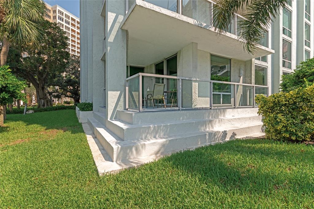 A ground-floor apartment patio with a glass railing and concrete steps leading to the lawn — 1111 N GULFSTREAM AVE #1A AVENUE UNIT 1A, SARASOTA, FL