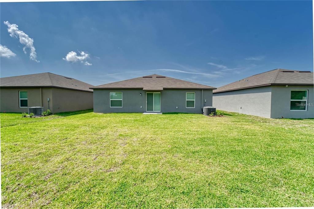 The exterior rear view of a single-story house features a grassy yard and sliding doors — 5514 BLUE AZURE DRIVE, WIMAUMA, FL