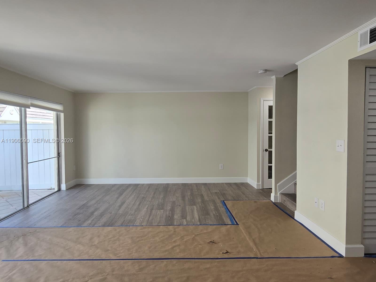 An empty room features light-colored walls, wood-look flooring, a sliding glass door, and protective paper — 6825 SW 45th Ln # 12, Miami FL 33155, MIAMI, FL